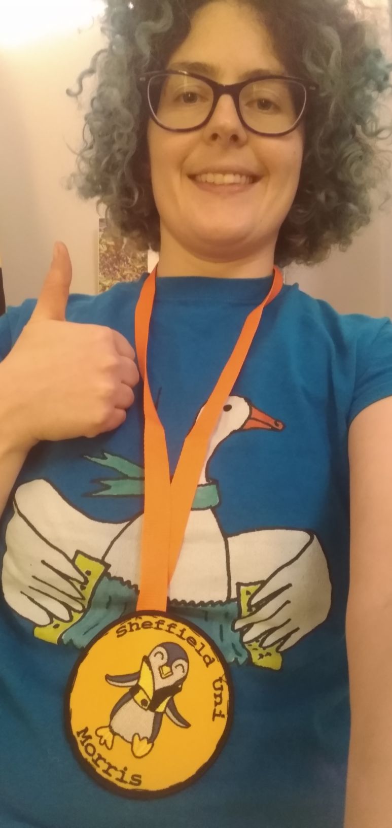 Sol wearing an orange committee lanyard, a big smile and holding a thumbs up!